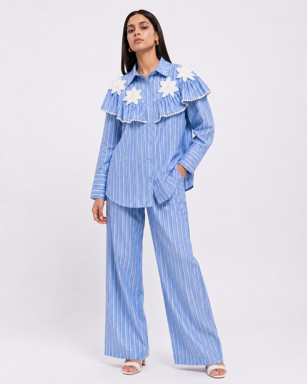 A blue striped co-ord set featuring statement layered frill detailing, delicate floral patch appliqués, and relaxed tailoring designed for effortless everyday dressing.